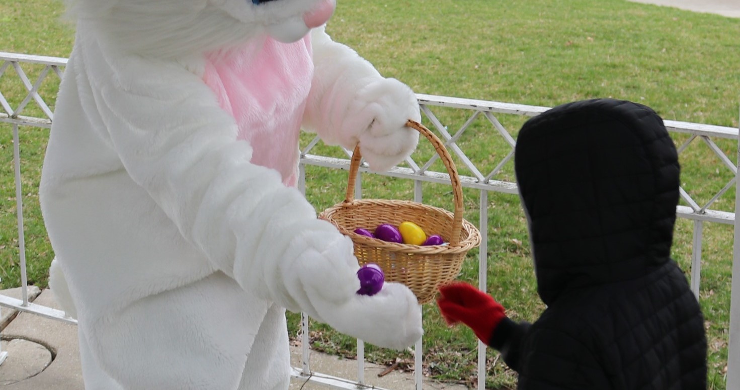 Easter bunny handing a kid an easter egg